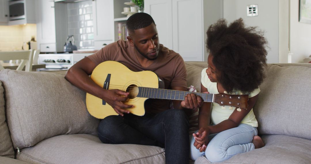 Father Teaching Daughter Guitar at Home on Comfortable Couch - Free Images, Stock Photos and Pictures on Pikwizard.com