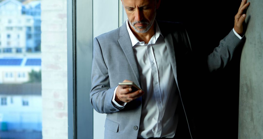 Businessman Checking Smartphone Near Window With Pensive Look - Free Images, Stock Photos and Pictures on Pikwizard.com