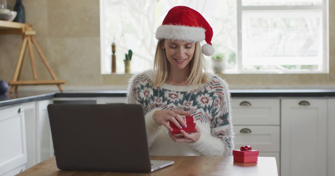 Smiling Woman in Santa Hat Opening Christmas Gift at Kitchen Table - Free Images, Stock Photos and Pictures on Pikwizard.com