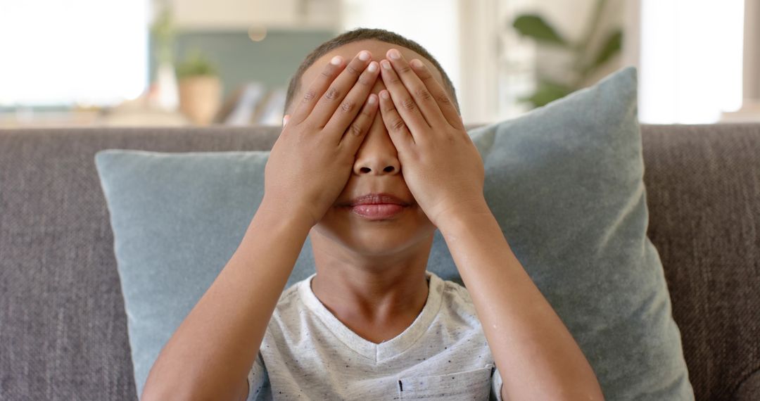 Boy Covering Eyes Sitting on Sofa with Cushions at Home