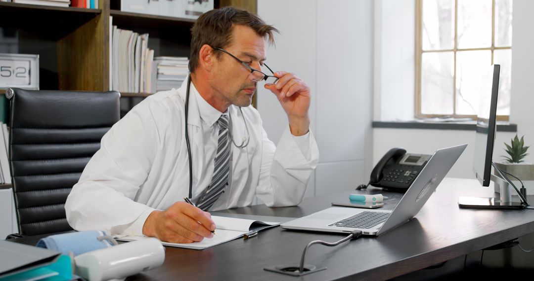 Middle-Aged Male Doctor Working in Office Checking Patient Records - Free Images, Stock Photos and Pictures on Pikwizard.com