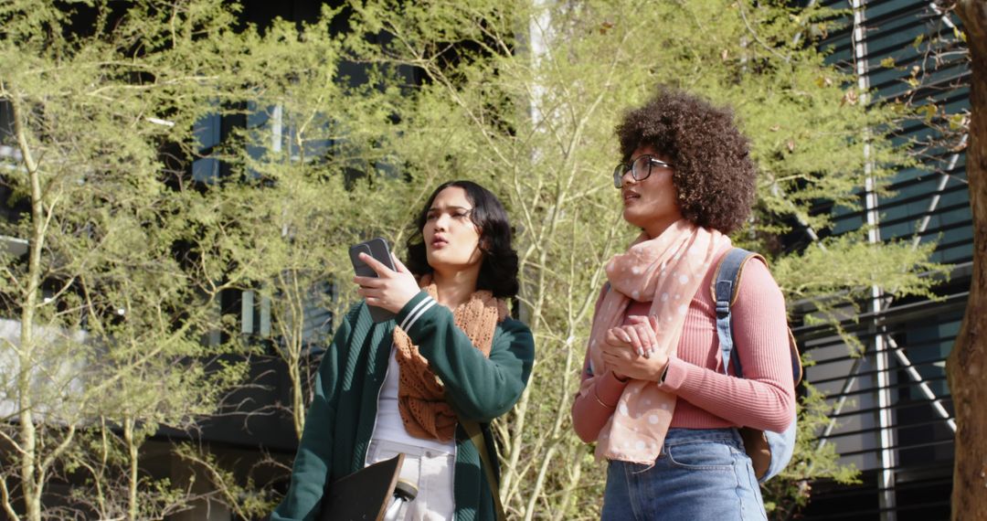 Young women navigating campus using smartphone with backpacks, scarves, and folders