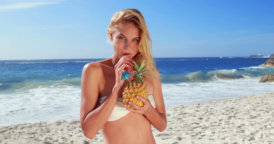 Attractive blonde drinking cocktail in pineapple at the beach - Free Images, Stock Photos and Pictures on Pikwizard.com