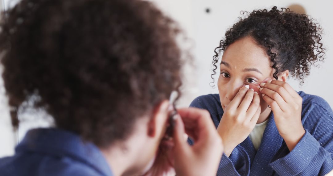 Young African American woman applying contact lens in bathroom mirror - Free Images, Stock Photos and Pictures on Pikwizard.com