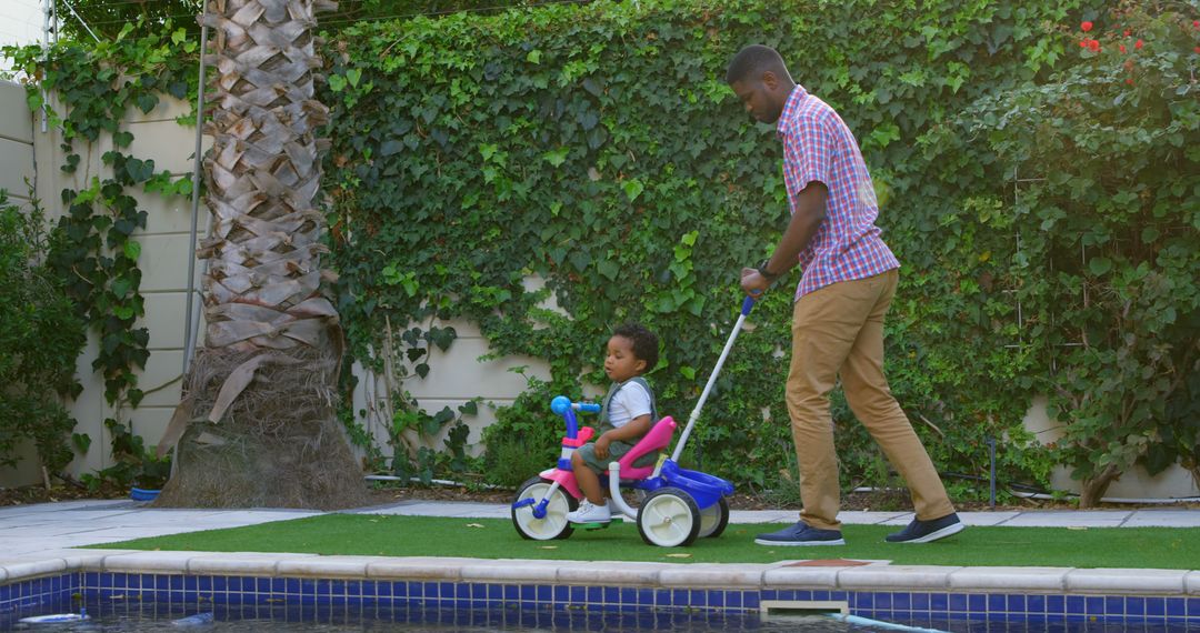 Father Spending Quality Time with Child Riding Tricycle by Pool - Free Images, Stock Photos and Pictures on Pikwizard.com