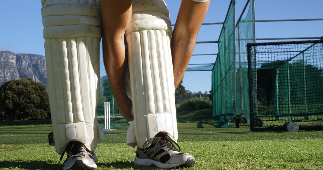 Cricketer Adjusting Shin Guards on Practice Field Under Sunny Skies - Free Images, Stock Photos and Pictures on Pikwizard.com