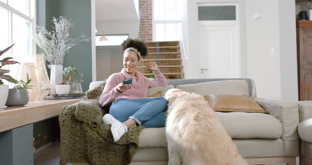 Biracial Woman Relaxing with Dog Using Smartphone at Home
