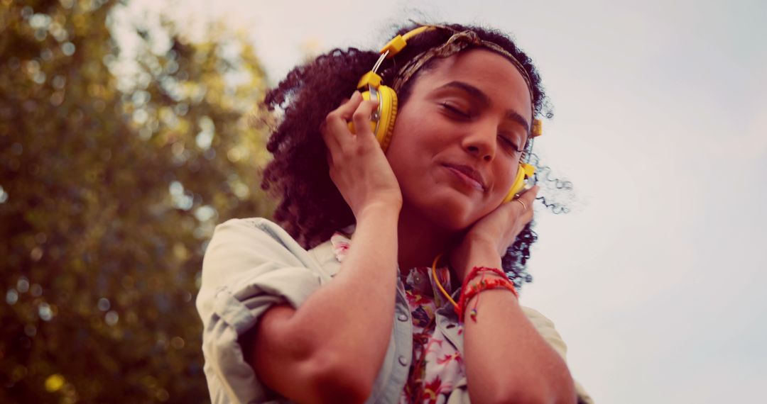 Young Woman Enjoying Music with Yellow Headphones Outdoors - Free Images, Stock Photos and Pictures on Pikwizard.com