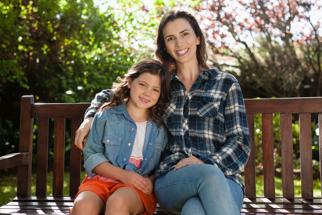 Portrait of smiling beautiful woman and daughter sitting on wooden bench - Free Images, Stock Photos and Pictures on Pikwizard.com