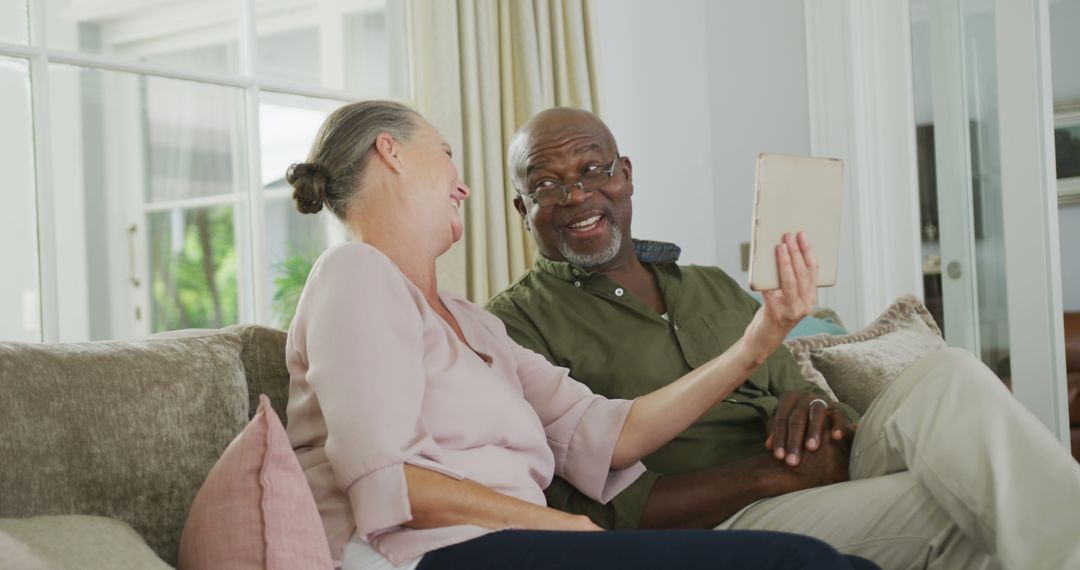 Joyful Senior Couple Enjoying Tablet on Couch