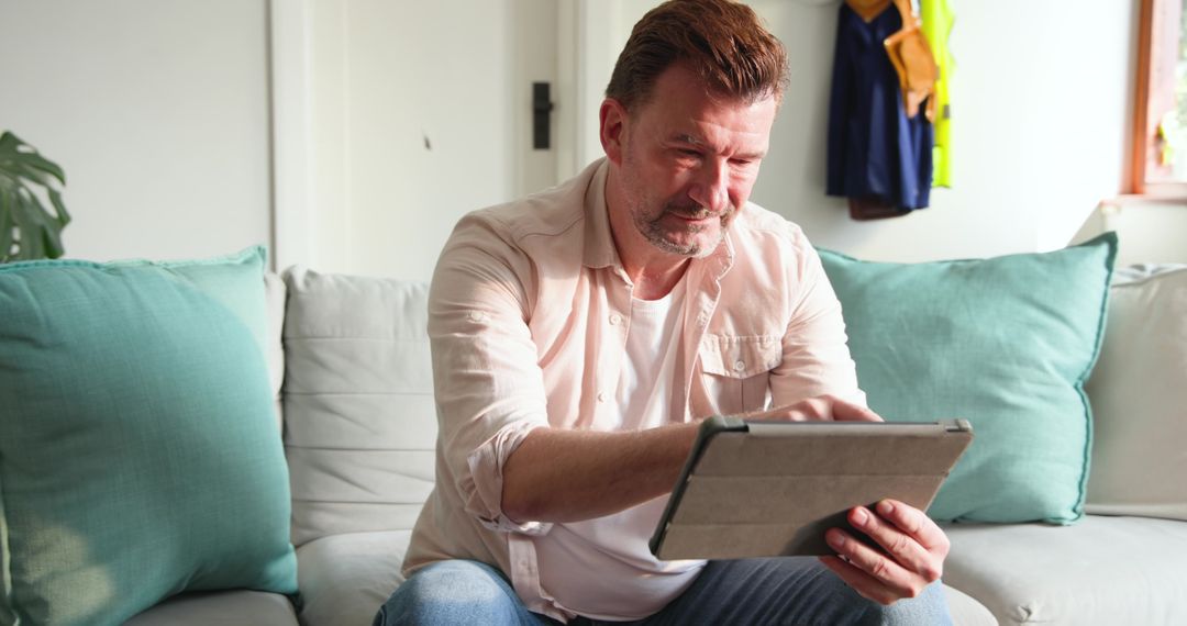 Middle-aged Man Relaxing at Home Using Tablet on Sofa