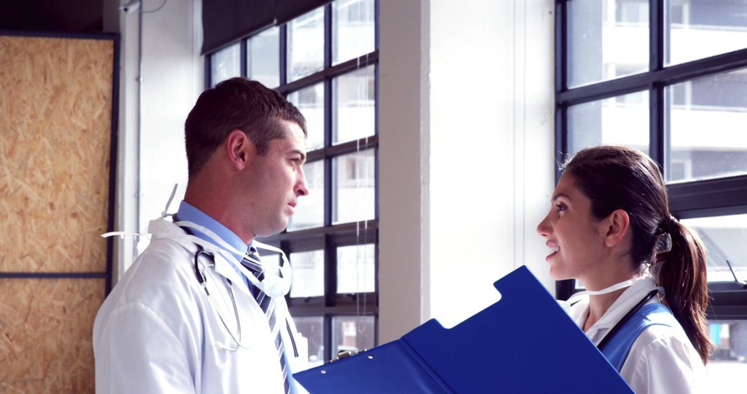 Medical Professionals Consulting Each Other Holding Medical Files Next to Windows - Free Images, Stock Photos and Pictures on Pikwizard.com