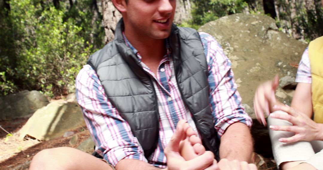 Man holding friend's foot while sitting outdoors in nature - Free Images, Stock Photos and Pictures on Pikwizard.com