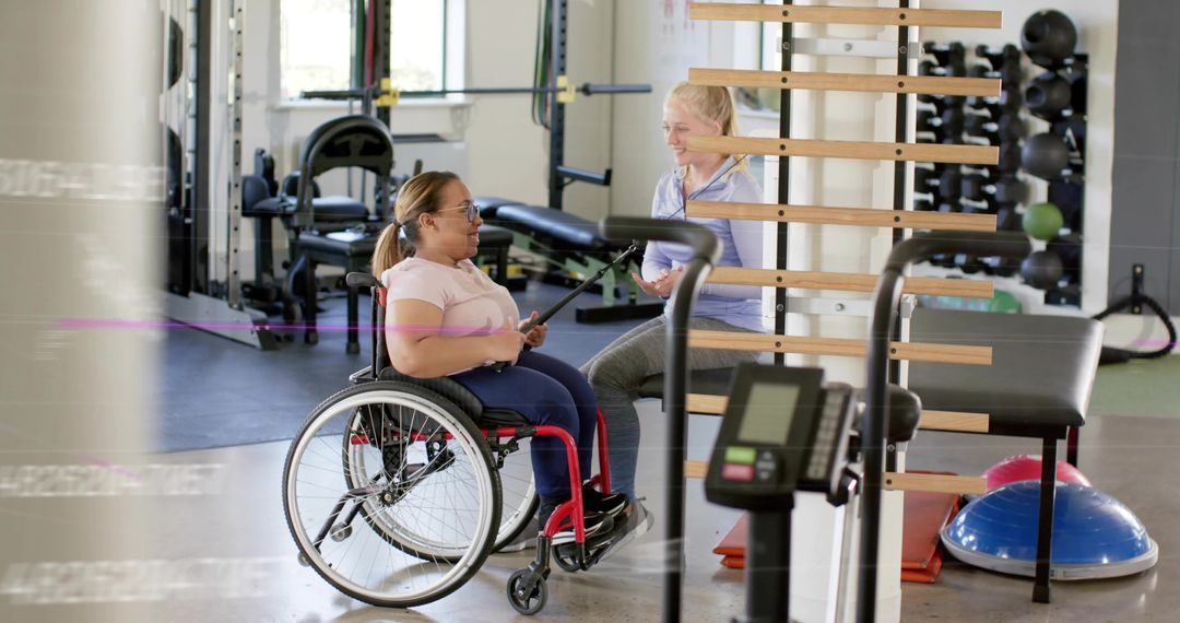 Wheelchair User Doing Resistance Band Workout with Coach Using Tablet in Bright Rehab Gym