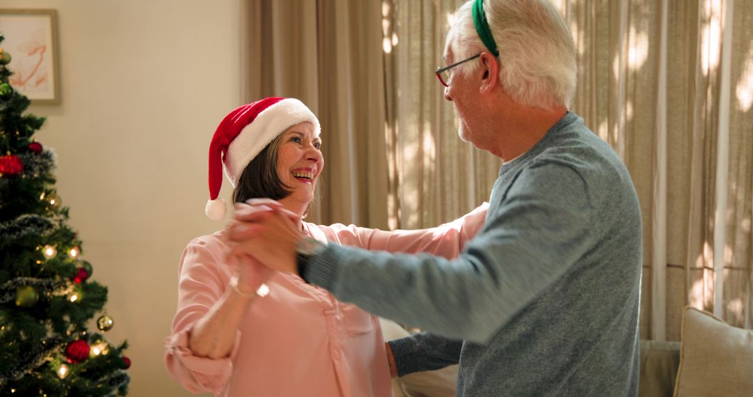 Senior Couple Dancing Joyfully by Christmas Tree with Festive Hats