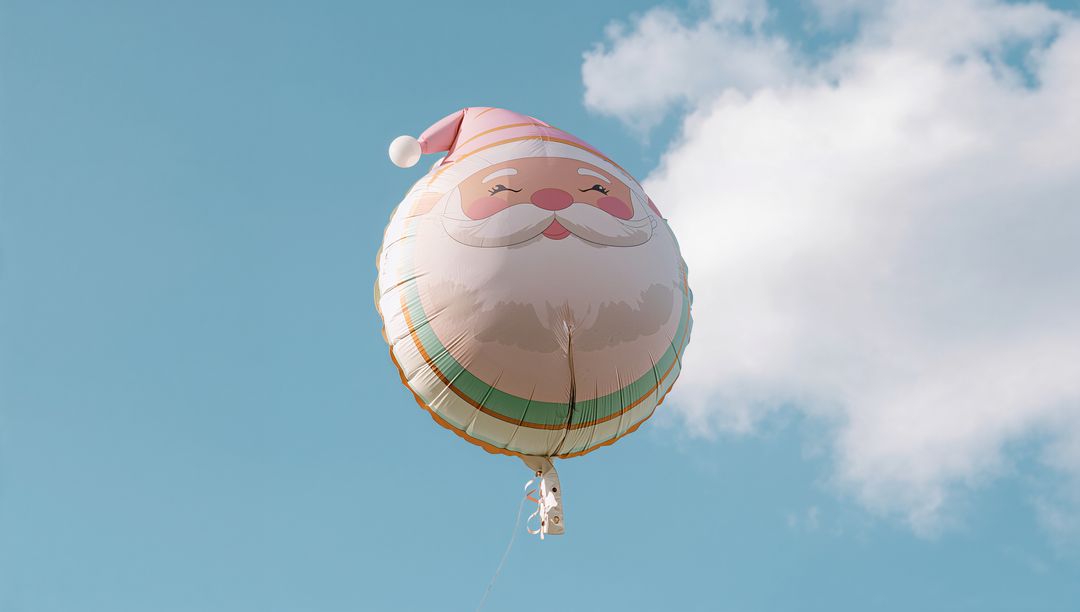 Floating round Santa balloon drifting across pale blue sky with soft cloud and thin tether ribbon