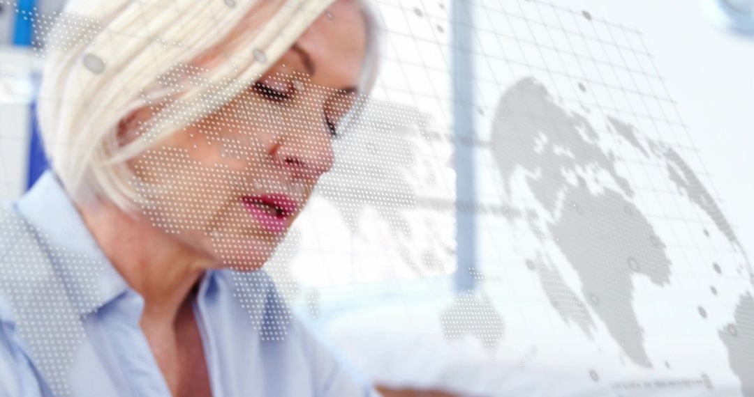 Senior professional reviewing global data with translucent world map overlay in office