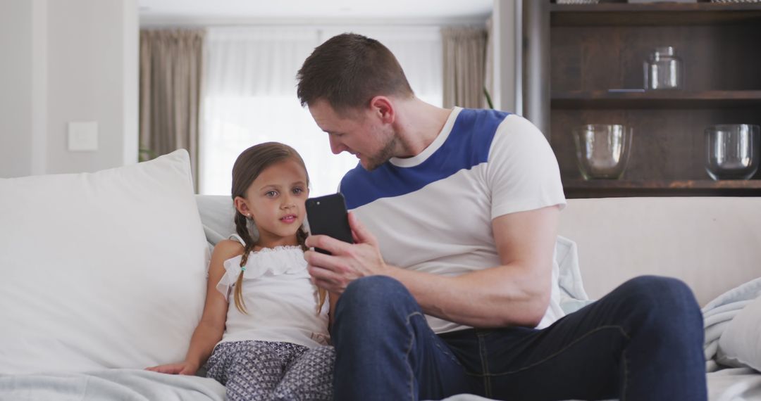 Father Showing Daughter Something on Smartphone in Living Room - Free Images, Stock Photos and Pictures on Pikwizard.com