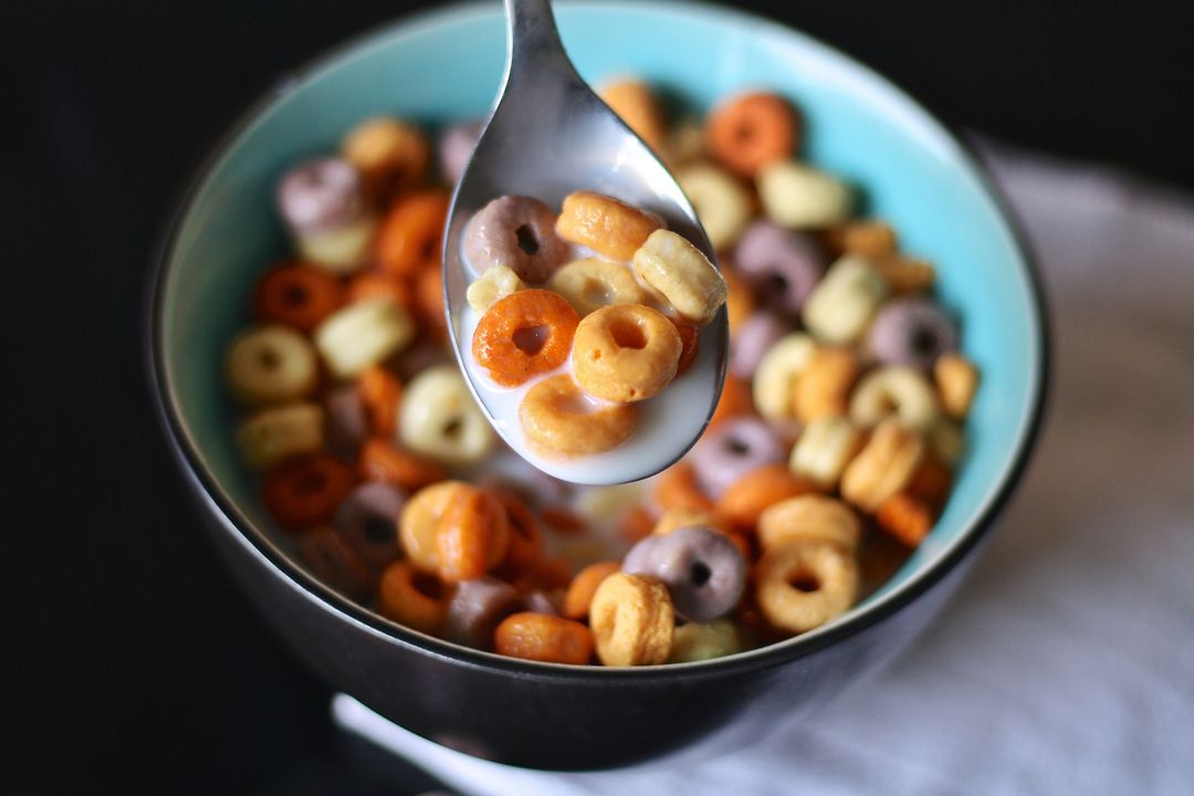 Metal Spoon Lifting Colorful Cereal Loops from Turquoise Bowl with Milk Splash