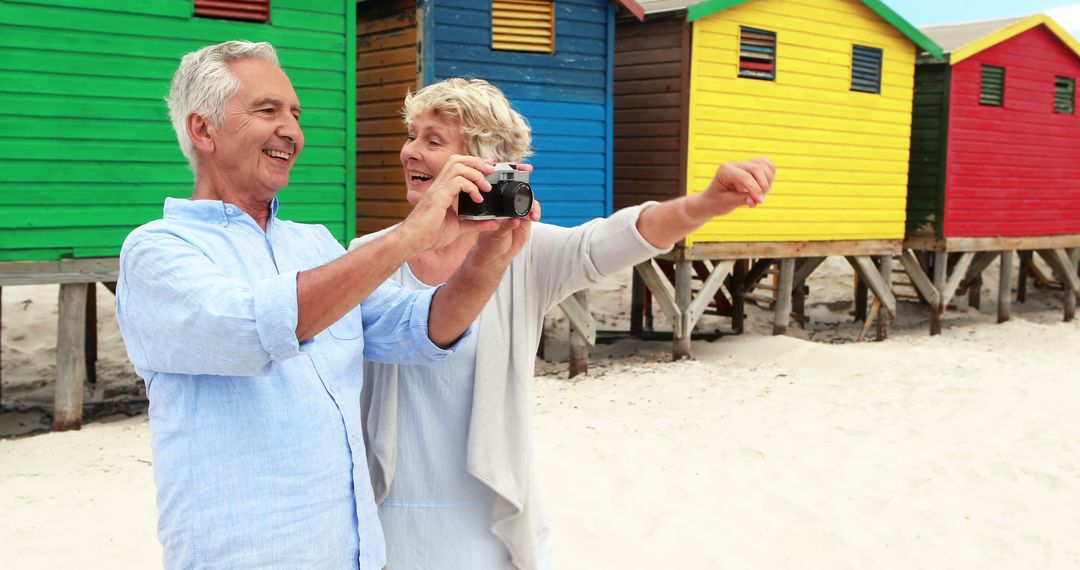 Senior Couple Taking Selfie on Beach with Colorful Beach Huts - Free Images, Stock Photos and Pictures on Pikwizard.com