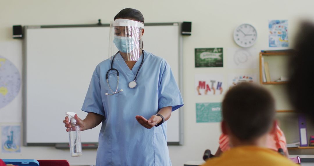 Biracial female medical worker wearing face mask showing schoolchildren how to disinfect hands - Free Images, Stock Photos and Pictures on Pikwizard.com