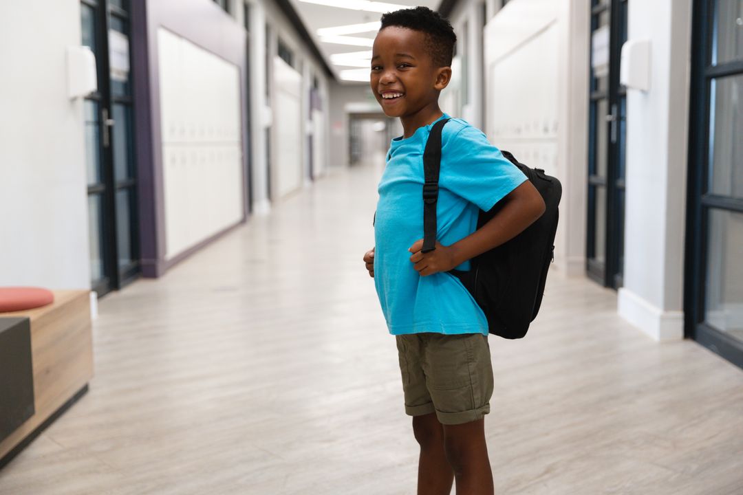 Happy african american elementary schoolboy with backpack standing in corridor - Free Images, Stock Photos and Pictures on Pikwizard.com