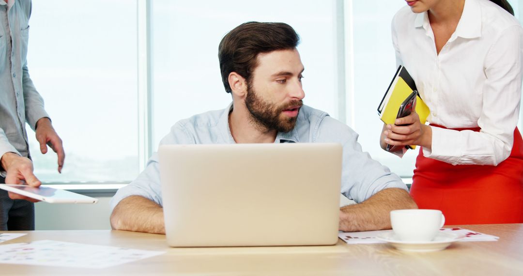 Stressed Businessman Working at Desk with Team Discussion