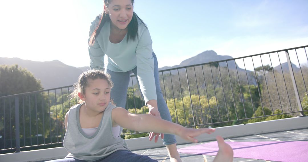 Mother helping daughter with yoga stretch on balcony with mountain view - Free Images, Stock Photos and Pictures on Pikwizard.com