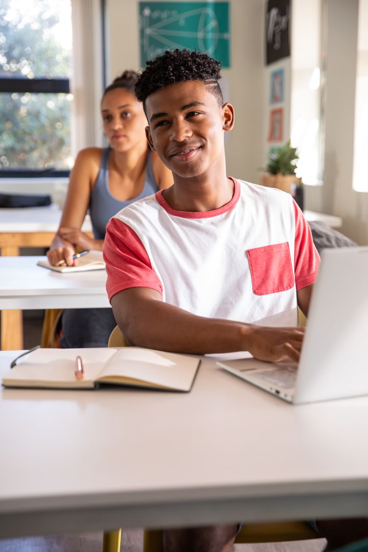 High school students studying together in bright classroom using laptop and taking notes