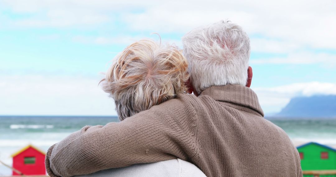 Elderly Couple Embracing by the Beach with Colorful Huts - Free Images, Stock Photos and Pictures on Pikwizard.com