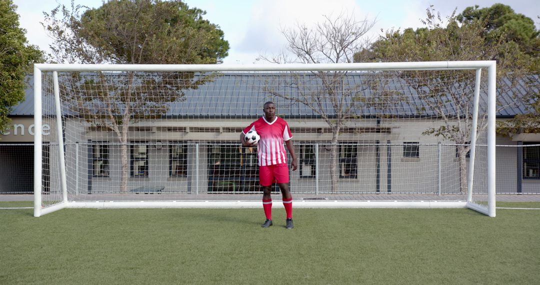 Soccer Player Standing Confidently in Front of Goal Holding Ball