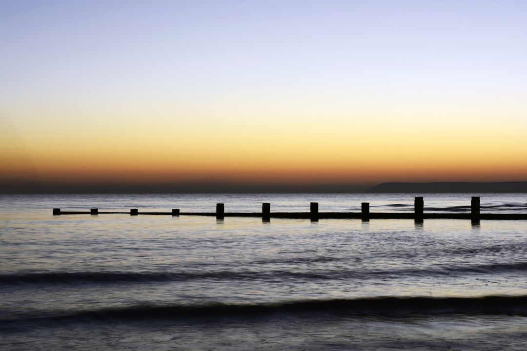 Serene Seaside Sunset with Tranquil Waves and Pier Silhouette - Free Images, Stock Photos and Pictures on Pikwizard.com