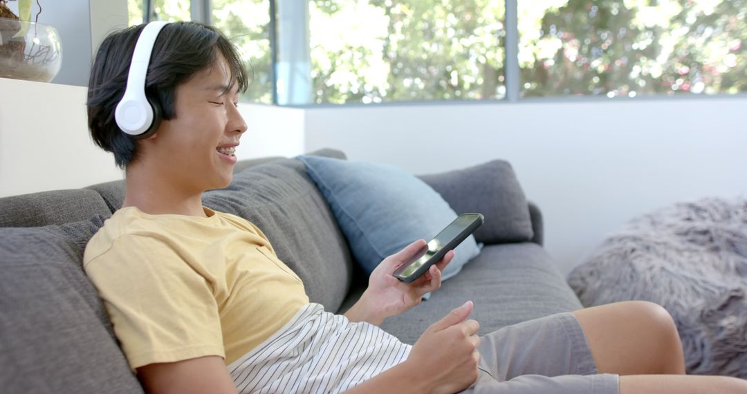 Asian Student Enjoying Music on Smartphone in Relaxing Home Setting