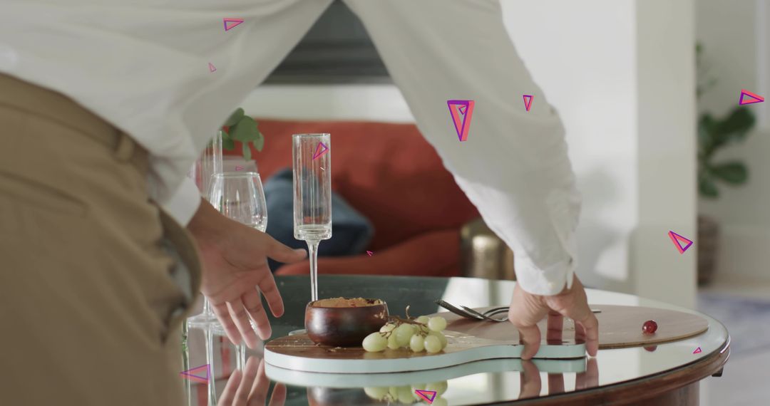 Man arranging elegant snack board with grapes and champagne flute on glass table