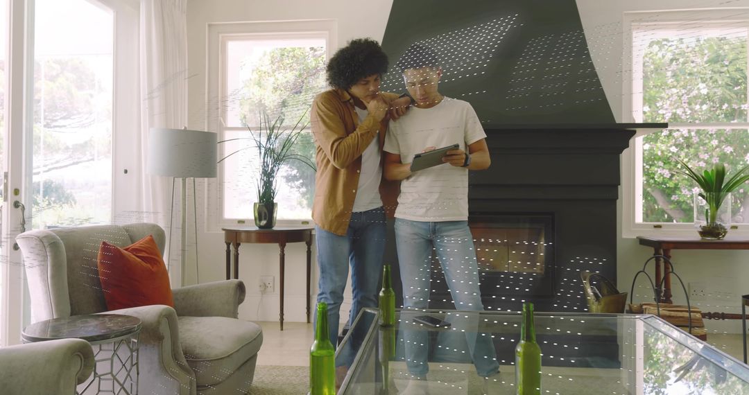 Two men leaning and pointing at tablet in modern living room with fireplace and plants