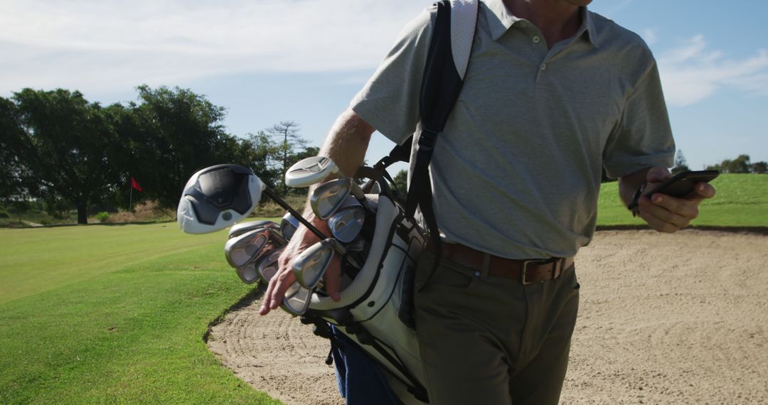 Golf Player Holding Clubs While Using Smartphone on Sandy Course