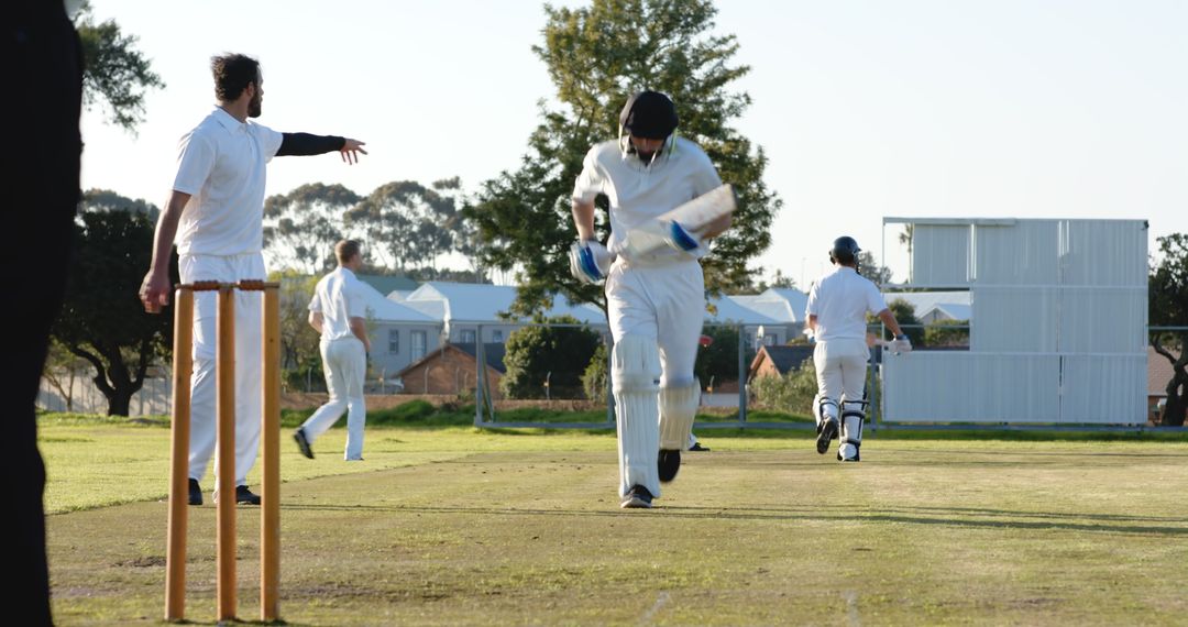 Cricket Players Running Between Wickets on Grass Field