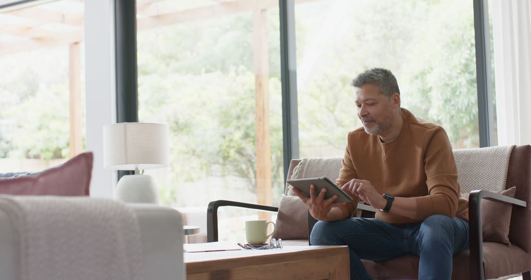 Middle-aged man using tablet in modern living room - Free Images, Stock Photos and Pictures on Pikwizard.com