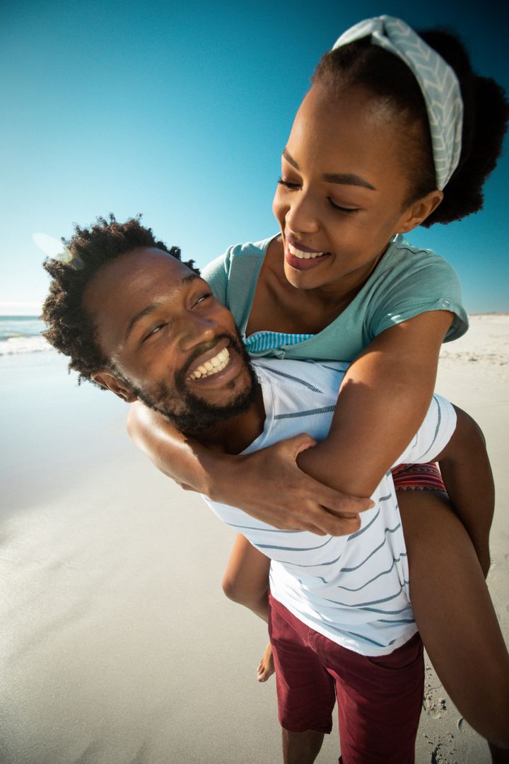 Happy African American Couple Piggybacking on Beach - Free Images, Stock Photos and Pictures on Pikwizard.com
