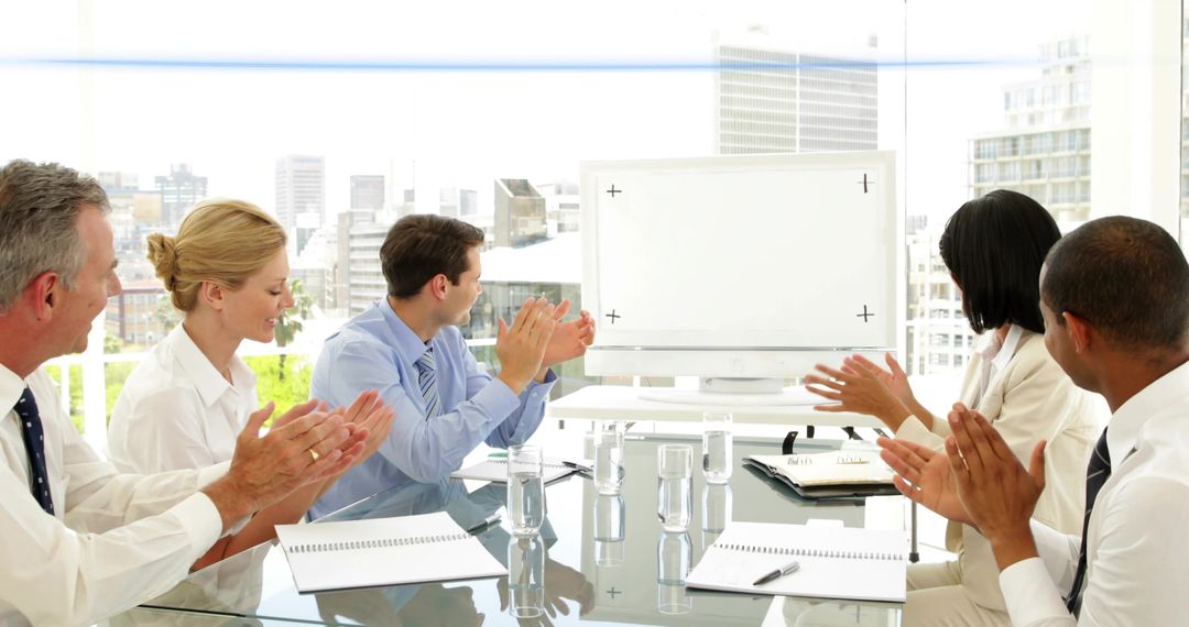 Business Team Applauding Around Glass Table with Blank Monitor and City Skyline View