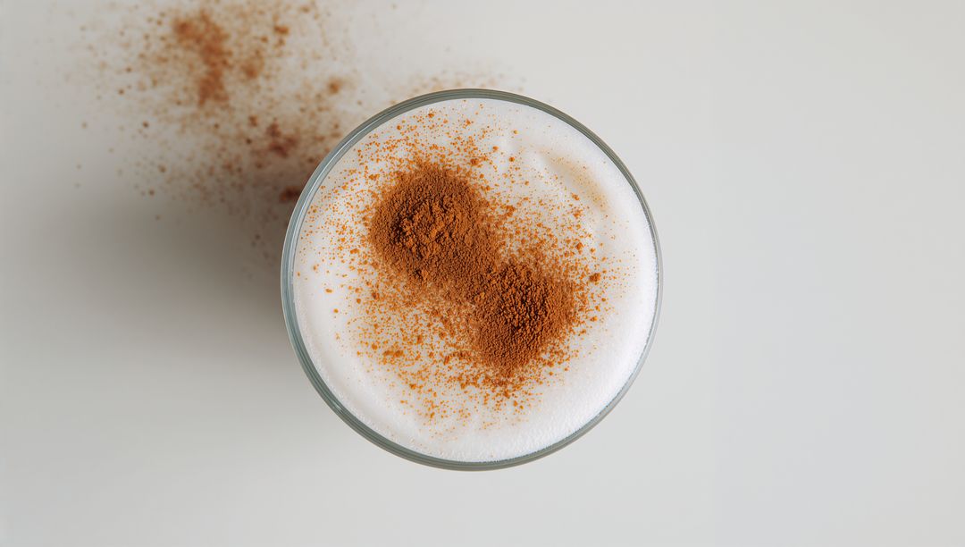 Top-Down Showing Cinnamon-Dusted Frothy Latte in Clear Glass Cup Minimalist Flatlay
