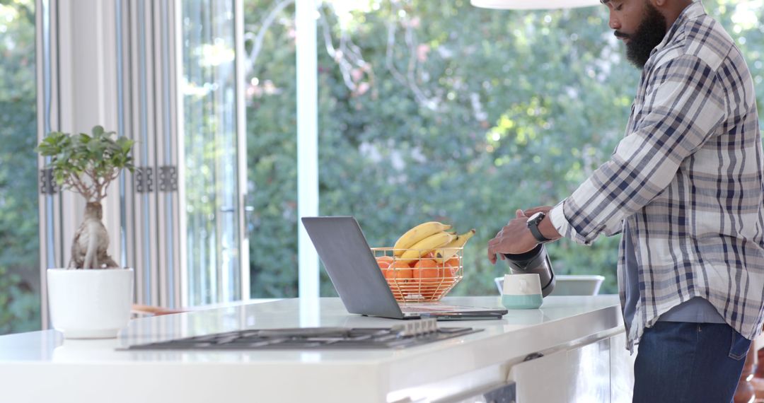 Man Preparing Breakfast in Modern Kitchen Next to Open Laptop - Free Images, Stock Photos and Pictures on Pikwizard.com