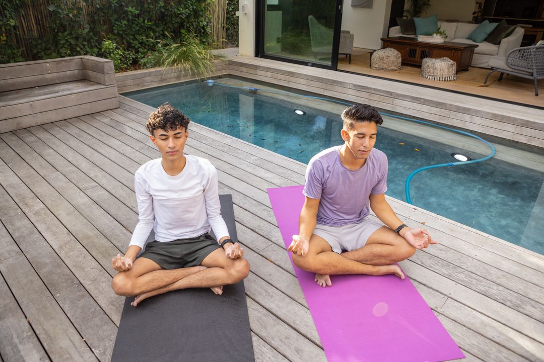 Young Men Meditating by Pool on Sunny Deck for Wellness and Mindfulness