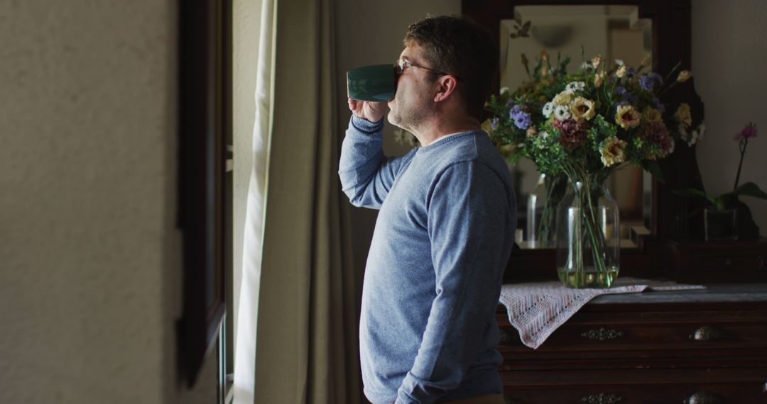 Man drinking coffee near window in cozy home interior - Free Images, Stock Photos and Pictures on Pikwizard.com