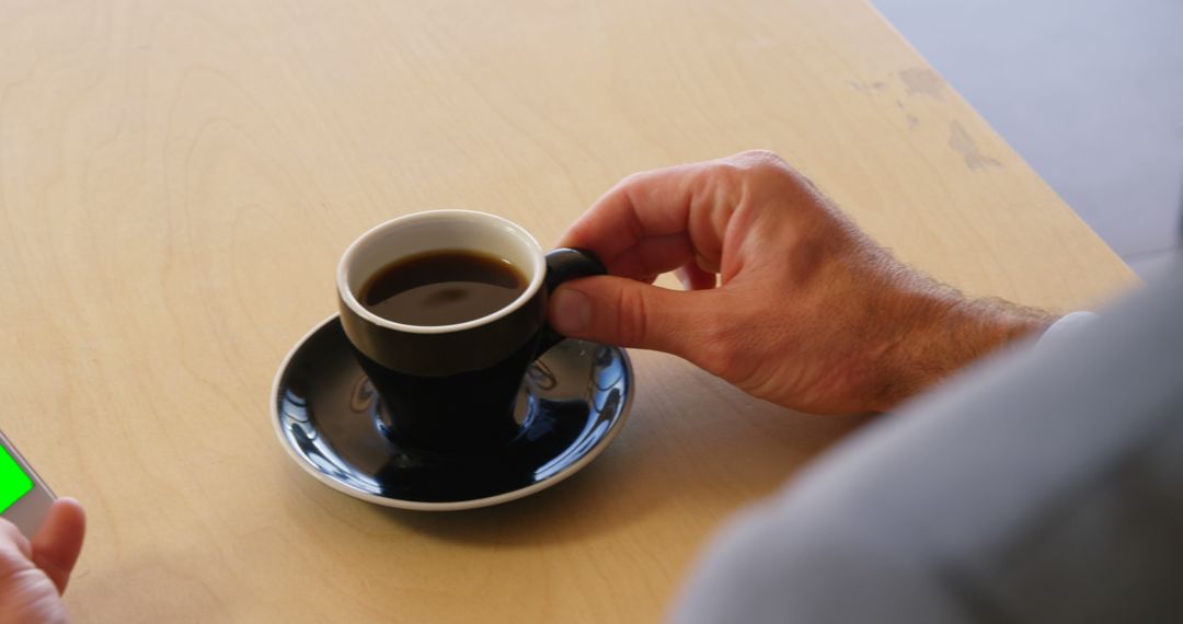 Man holding coffee cup while using smartphone at table - Free Images, Stock Photos and Pictures on Pikwizard.com
