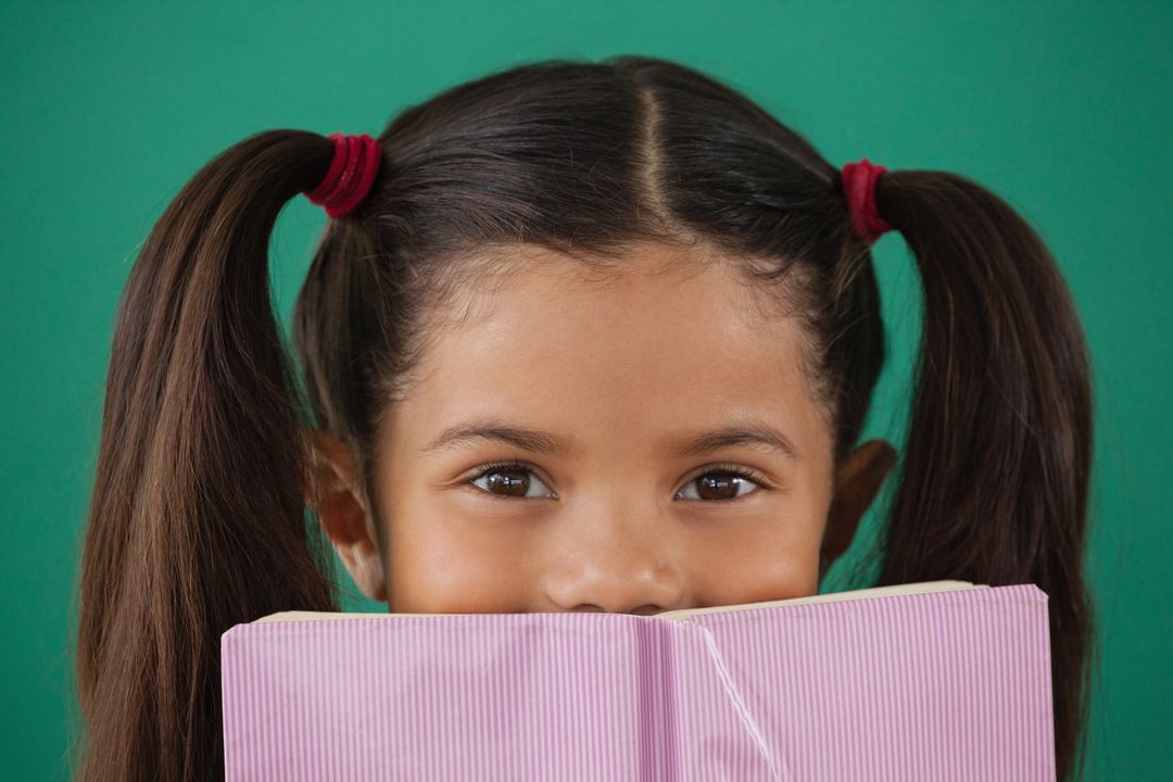 Schoolgirl hiding behind a book against green background - Free Images, Stock Photos and Pictures on Pikwizard.com