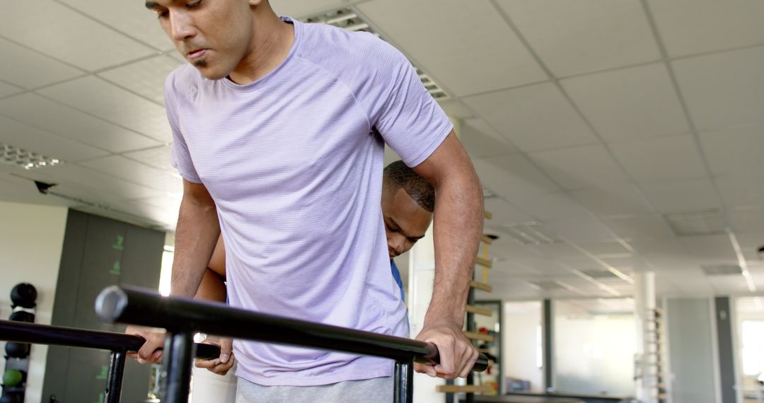 Man in Rehabilitation with Therapist in Gym Using Parallel Bars