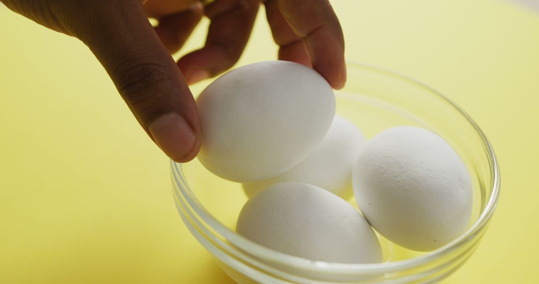 Hand Reaching for Eggs in Glass Bowl on Yellow Background - Free Images, Stock Photos and Pictures on Pikwizard.com