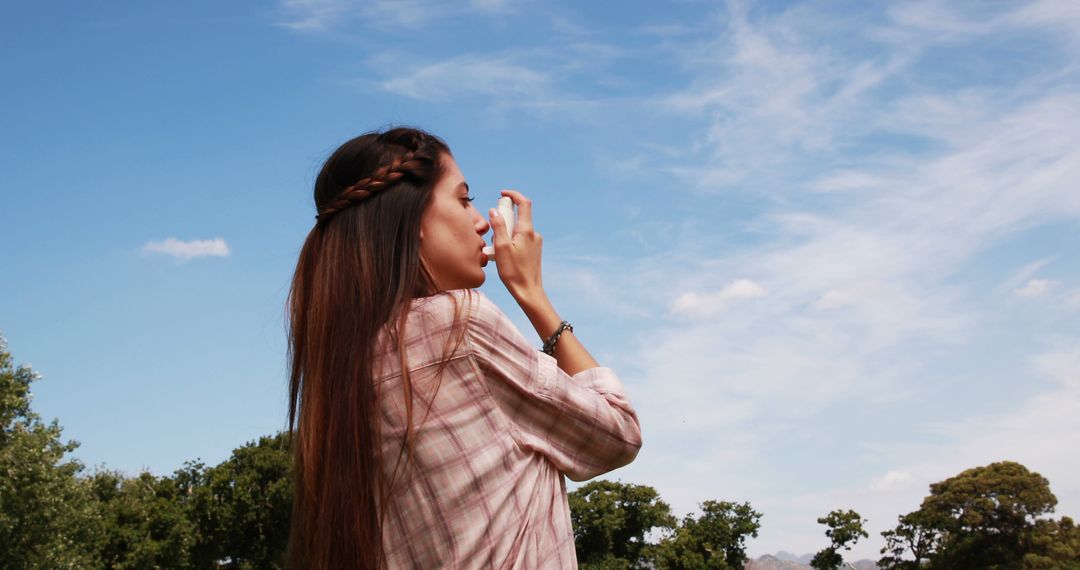 Woman Using Inhaler Under Clear Blue Sky for Asthma Relief - Free Images, Stock Photos and Pictures on Pikwizard.com