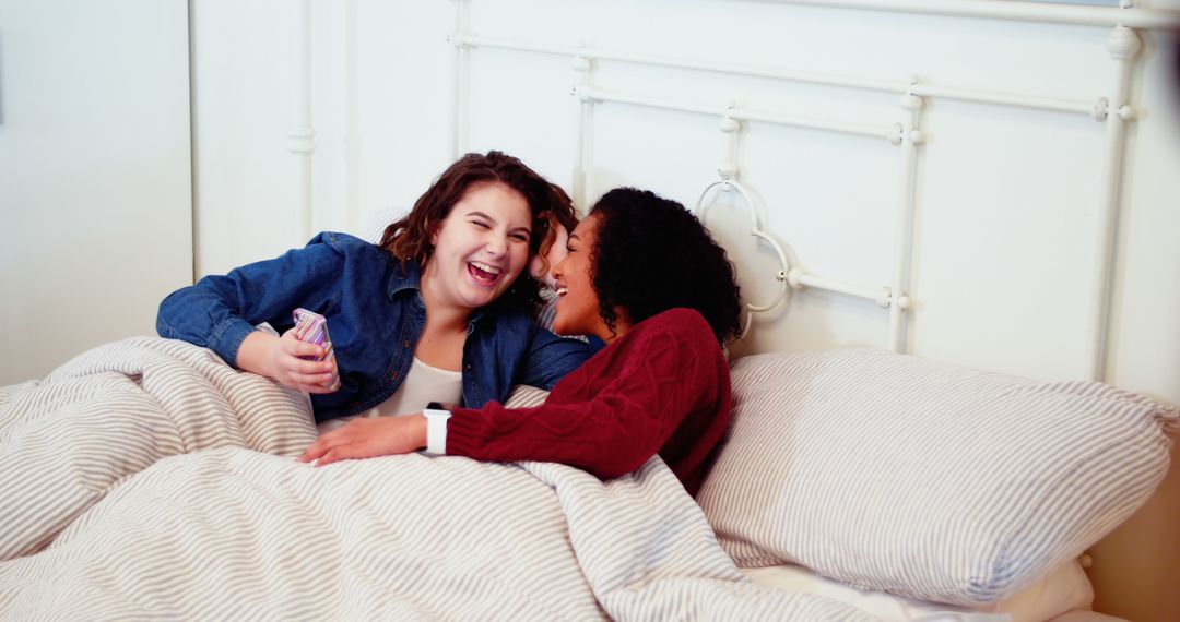 Happy Lesbian Couple Relaxing in Bed Using Mobile Phone